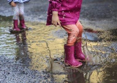 Neşeli çocuk yağmur sonrası su birikintisine atlıyor.