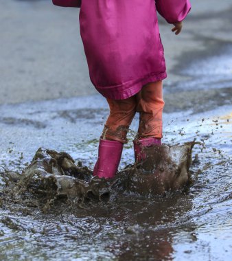 Neşeli çocuk yağmur sonrası su birikintisine atlıyor.