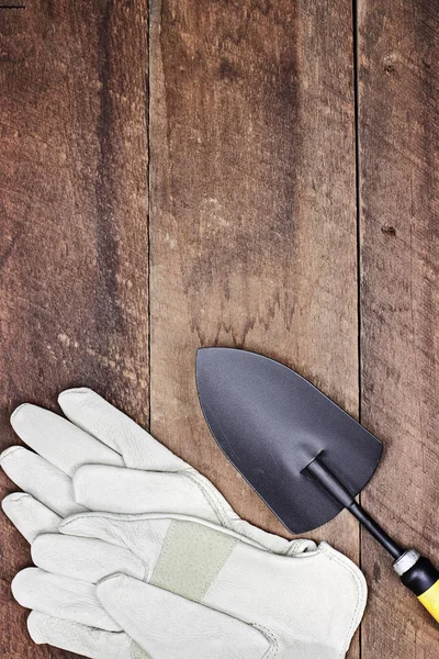 Garden gloves and hand spade over a rustic wooden table. Image shot from above in flat lay style.