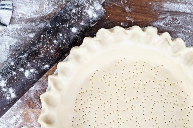 Ev yapımı tereyağı pasta kabuk pasta plaka yivli boğumlu kenar, oklava ile hamur unlanmış rustik ahşap arka plan üzerinde ek top. Kabuk delikli çatal ile ve pişirme için hazır oldu.