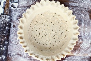 Ev yapımı tereyağı pasta kabuk pasta plaka yivli boğumlu kenar, oklava ile hamur unlanmış rustik ahşap arka plan üzerinde ek top. Kabuk delikli çatal ile ve pişirme için hazır oldu.