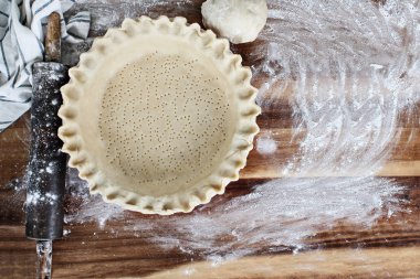 Ev yapımı tereyağı pasta kabuk pasta plaka yivli boğumlu edge, oklava, havlu ve hamur unlanmış rustik ahşap arka plan üzerinde ek top ile. Kabuk delikli çatal ile ve pişirme için hazır oldu.