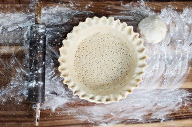 Ev yapımı tereyağı pasta kabuk pasta plaka yivli boğumlu kenar, oklava ile hamur unlanmış rustik ahşap arka plan üzerinde ek top. Kabuk delikli çatal ile ve pişirme için hazır oldu.