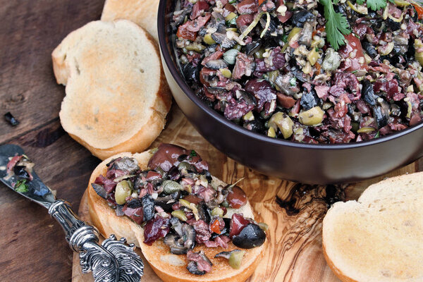 Homemade mixed Olive Tapenade made with garlic, capers, olive oil, Kalamata, black and green olives spread over toasted bread. Image shot from above.