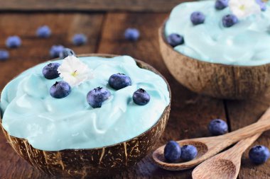 Mavi spirulina ve meyve güler yüzlü kase, tahta kaşık Hindistan cevizi kaseler rustik bir arka plan üzerinde beyaz çiçeklerle hizmet ile taze meyve. 