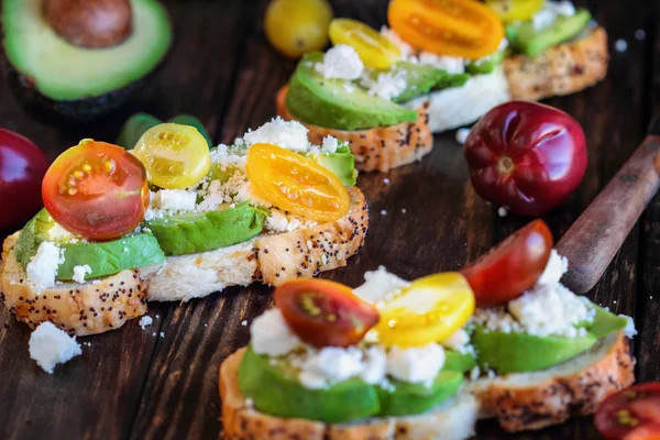 Avocado toast sandwich with avocados, fresh from the garden heirloom tomatoes and feta cheese, Greek food and healthy vegetarian diet concept, over a rustic wooden background.