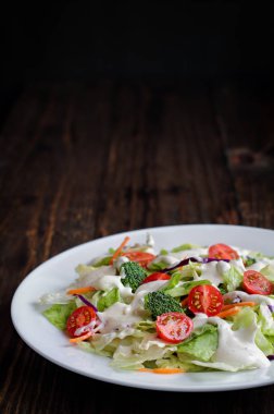 Ev yapımı taze salata ayran Çiftlik sosu, domates, brokoli, lahana ve havuç bir rustik ahşap masa ve koyu arka plan üzerinde saçtan. Ev salatası.