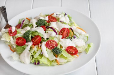 Ev yapımı taze salata ayran Çiftlik sosu, domates, brokoli, lahana ve havuç ile tabak Beyaz ahşap masa üzerinde servis. Ev salatası.