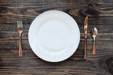 Beyaz yemek tabağı bir rustik ahşap masa üzerinde boş / çatal, bıçak ve kaşık arka plan... Üstten Görünüm. 