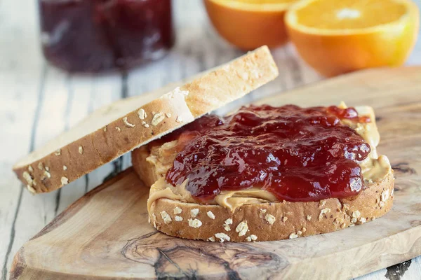 Homemade Peanut Butter and Jelly Sandwich on oat bread, over a rustic wooden background with fruit in the background ready for lunch.