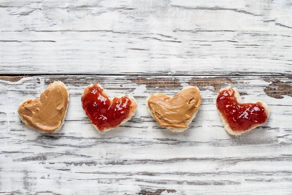 Top view of open face homemade peanut butter and jelly heart shaped sandwiches over a white rustic white wooden table / background. Top view.