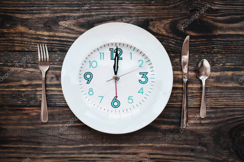 Twelve hour intermittent fasting time concept with clock on plate over a rustic wooden table / background. Top view. 