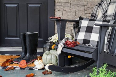 Sonbahar için geleneksel veranda yağmur botları, aile yadigarı kabaklar, beyaz balkabakları, anneler ve bizon yastıklı sallanan sandalye ile süslenmiş ve davetkar bir atmosfer veren bir battaniye fırlatılıyor..