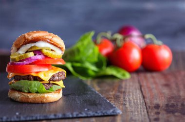 Büyük, yağlı, sulu bir çift çizburger% 100 sığır eti köftesi, erimiş peynir, soğan, turşu, marul, domates ve mayonez dilimleri ile yapılmış. Bulanık arkaplan ile sığ alan derinliği.