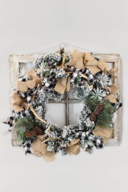 Ev yapımı ülke ya da avcıların Noel çelengi gri bir duvardaki kırsal çiftlik evinin camında. Çam kozalakları, köknar dalları, bufalo ekose kurdelesi, çuval bezi ve geyik boynuzu yaptım. Sahte kar yığını. Boşluğu kopyala.