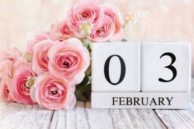 3 Şubat tarihli beyaz tahta takvim blokları ve ahşap bir masanın üzerinde pembe ranunculus çiçekleri. Bulanık arkaplan ile seçmeli odak. 