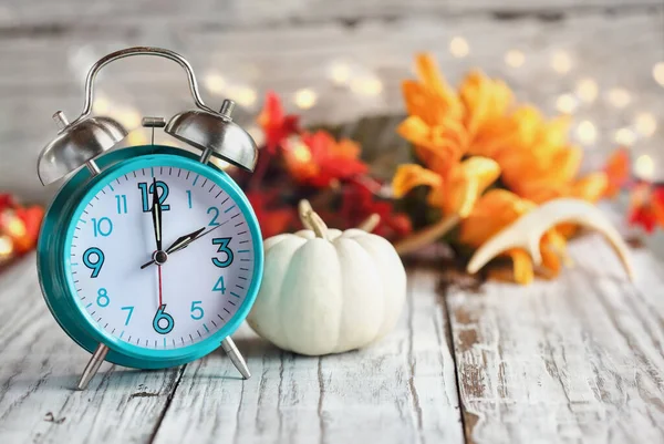 時計をセットし 戻って落ちる 白い木製のテーブルの上にミニカボチャ カラフルな秋の葉 釣り人やボケライトの時計や装飾 昼間の時間節約の概念 — ストック写真