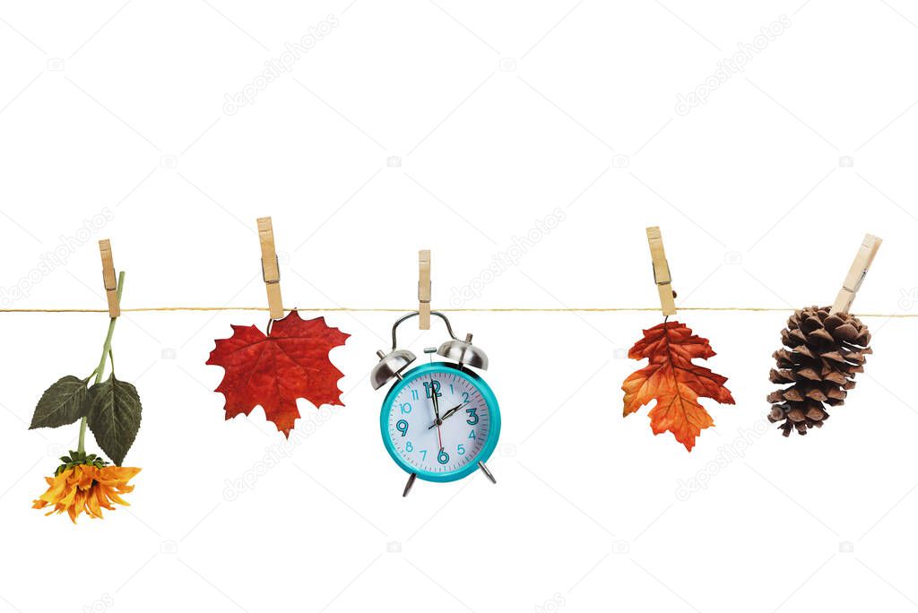 Set your clocks back with this clock, flower, autumn leaves and and pine cone hanging by clothes pins to a clothes line over a white background. Daylight saving time concept. Clipping path included.