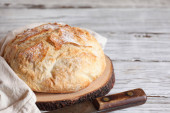 Čerstvý domácí řemeslný chléb na řezací desce s ručníkem a nožem.