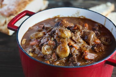 Beef Bourguignon cooked in an enameled cast iron Dutch oven and served with homemade artisan bread over a rustic wood background. clipart