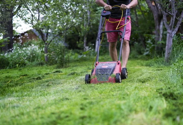 Un hombre cortando la hierba con una cortadora de césped — Foto de Stock