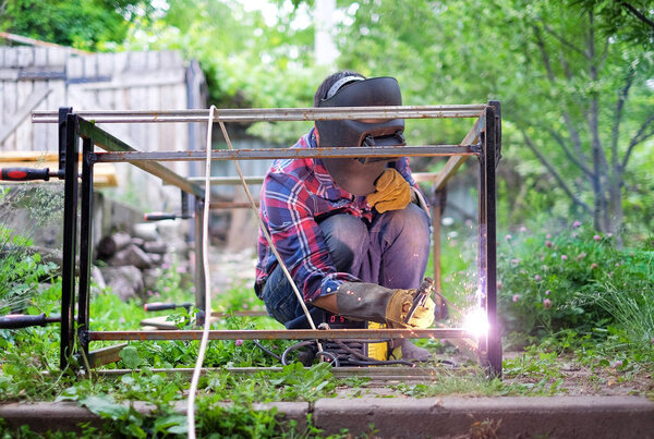 Человек в защитной маске сварки металлической конструкции на улице в летний день
.