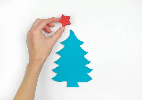 A hand decorating little wooden christmas tree with a star, white background. Flat lay. Top view. — Stock Photo, Image
