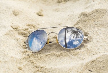 Aynalı güneş gözlükleri, kumsala yakın, palmiye ağaçlarının yansımasıyla.