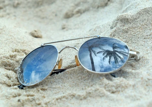Дзеркальні сонцезахисні окуляри крупним планом на пляжному піску з відображенням пальм — стокове фото