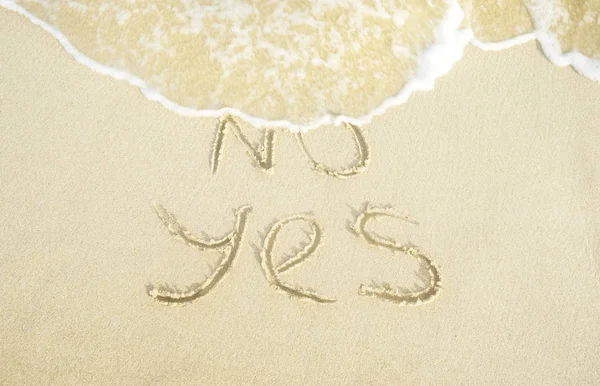 Say yes to life. No and Yes words written on the sand where No is getting washed away by the wave