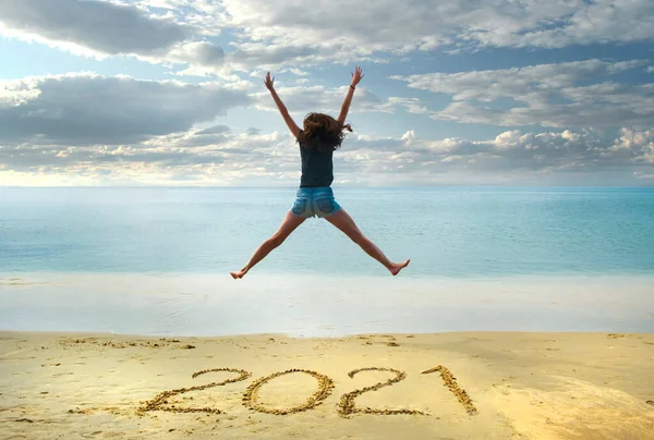 Año Nuevo 2021 escrito en la arena, chica feliz con las manos arriba saltando en la playa —  Fotos de Stock