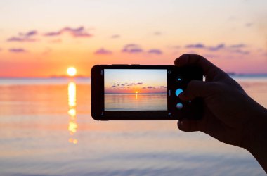 Cep telefonuyla deniz üzerinde gün batımının resmi