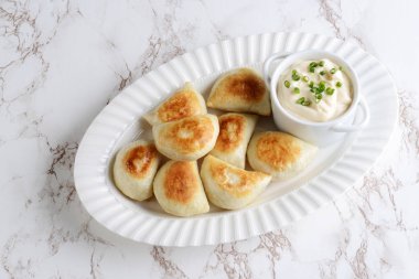 ekşi krema ve taze soğan ile beyaz bir tepside üstten görünüm börek