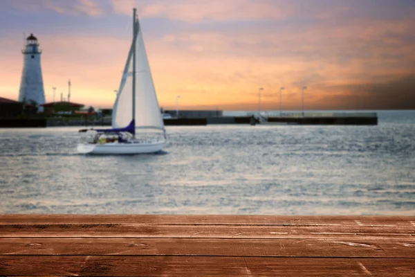 wood deck with sailboat and lighthouse at sunset