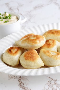 bir tabak üzerinde ekşi krem ve bahar soğan ile pierogi yığını