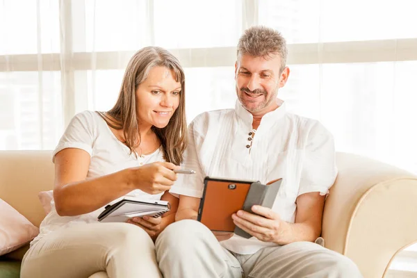 タブレットとメモ帳付きのアパートのソファの上の夫と妻 — ストック写真