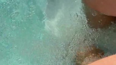 Yüzme havuzundaki su altı masaj jetlerinin yakın çekimi, insan bacakları etrafında kaynayan su. Hidroterapi, sağlık ve rahatlama konsepti