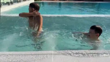 Güneşli bir günde açık havuzda oynayan ve yüzen üç genç çocuk. Yaz eğlencesi, çocuklar suyun tadını çıkarıyor ve birlikte gülüyorlar. Aile tatil sahnesi