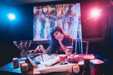 Stüdyoda iş yerinde genç sanatçı. Arka planda büyük tuval