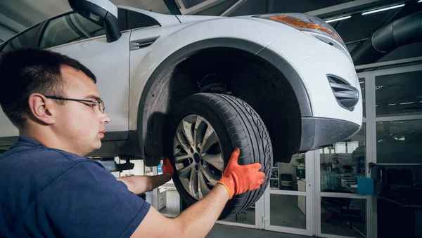 Car mechanic inspecting wheel and suspension detail of lifted automobile at repair service station. Auto service.