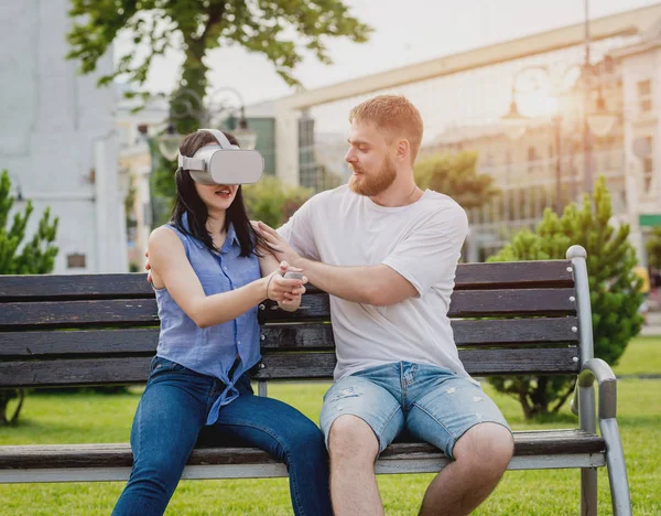 Young caucasian couple plays a game using virtual reality glasses on the street. VR headset.