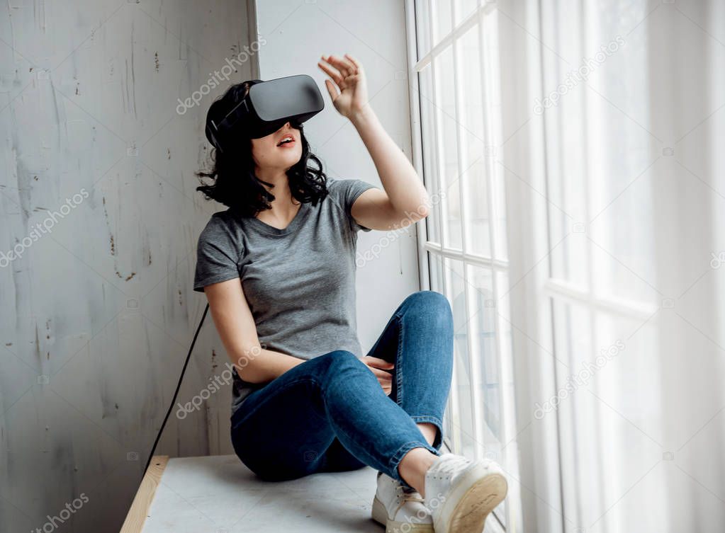 Young girl wearing virtual reality goggles sitting by the window