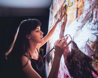 Stüdyoda iş yerinde genç sanatçı. Arka planda büyük tuval