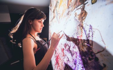 Stüdyoda iş yerinde genç sanatçı. Arka planda büyük tuval