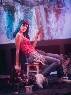 Stüdyoda iş yerinde genç sanatçı. Arka planda büyük tuval