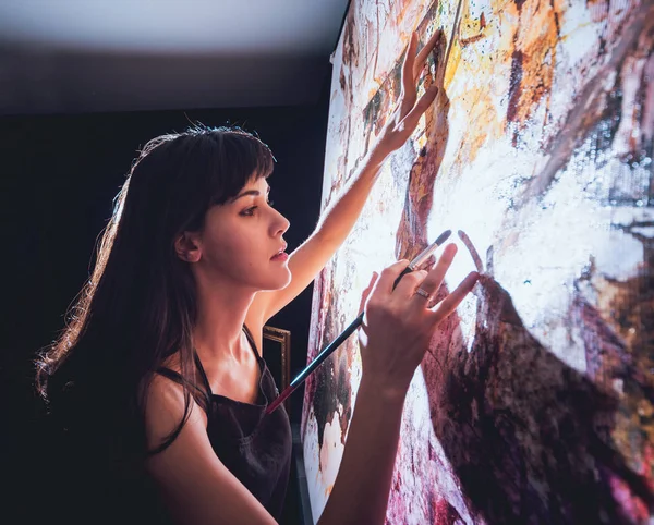 Stüdyoda iş yerinde genç sanatçı. Arka planda büyük tuval