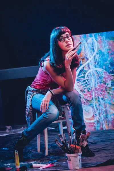 Stüdyoda iş yerinde genç sanatçı. Arka planda büyük tuval