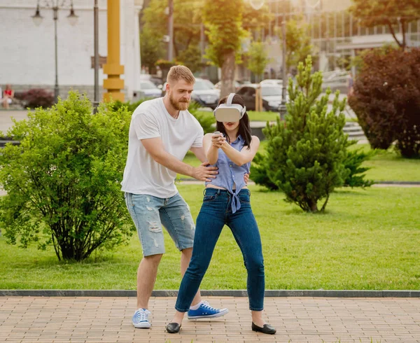 Young caucasian couple plays a game using virtual reality glasses on the street. VR headset.