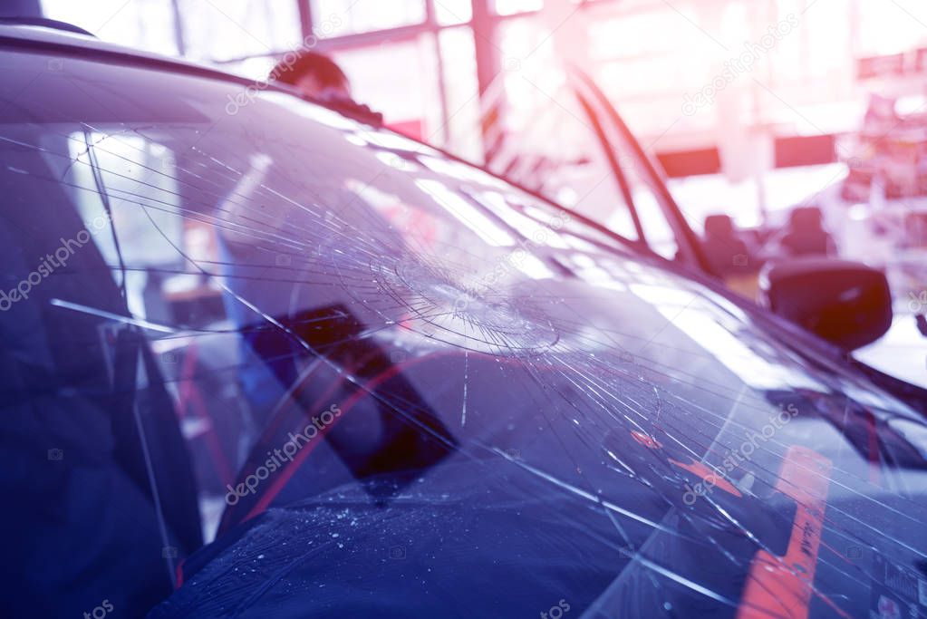 Automobile special workers remove old windscreen or windshield of a car in auto service station garage. Background