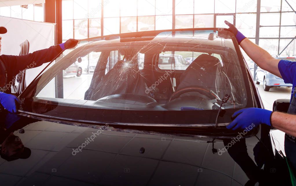 Automobile special workers replacing windscreen of car in auto service station garage